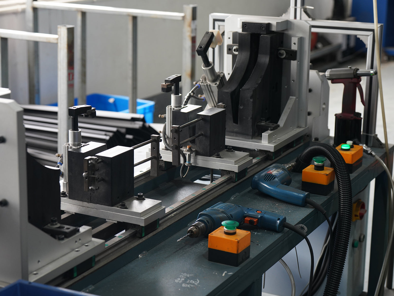Industrial machinery on a production line with metal frames, black components, orange and green control boxes, and handheld power tools on a conveyor table.